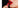Glossy blood-red lips against a dark background, a hand applying red lipstick