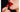 Glossy blood-red lips against a dark background, a hand applying red lipstick